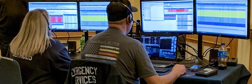 Emergency telecommunicators take calls at a desk with multiple monitors.