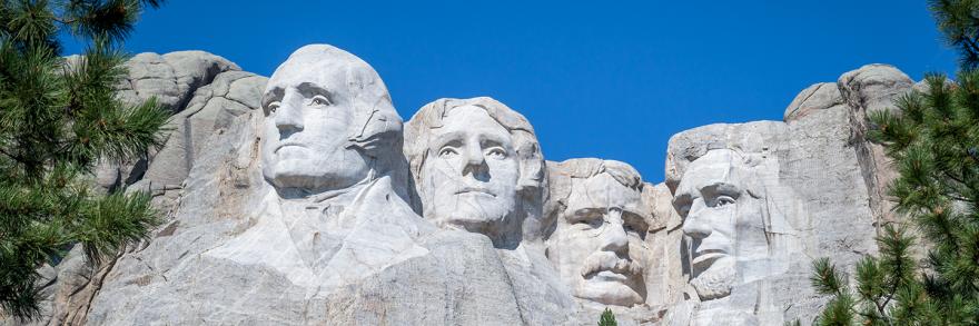 Framed on either side by tree branches, Mount Rushmore from below on a clear day with no clouds. 