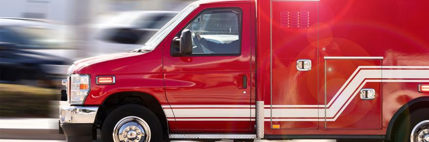 Red ambulance in motion with blurred road in background.