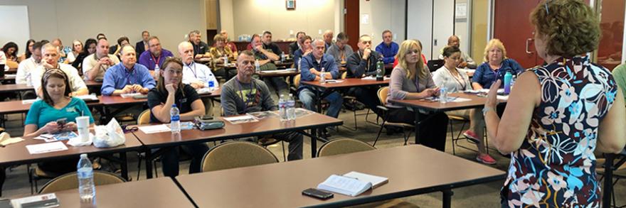 FirstNet Authority Senior Public Safety Advisor Kristi Wilde speaks in front of a group of emergency communications professionals seated behind desks 
