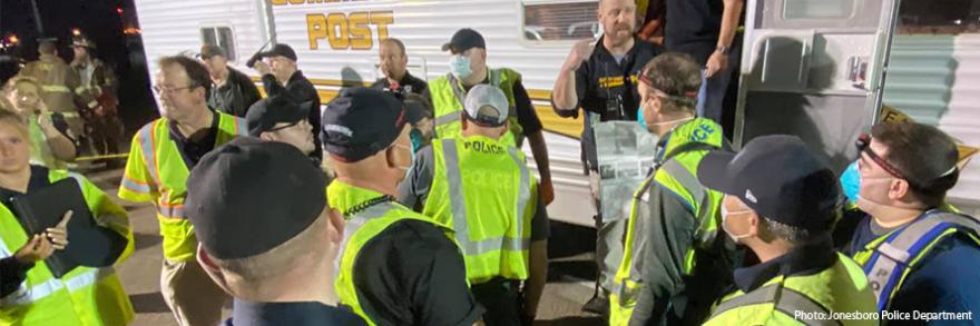 A group of first responders wearing yellow vests and medical masks gather outside an emergency response vehicle preparing to assist after a tornado near Jonesboro, Arkansas