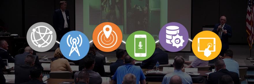 Six icons representing the Roadmap domains connected by a line over an image of two FirstNet Authority staff speaking to an audience of law enforcement and fire services representatives.