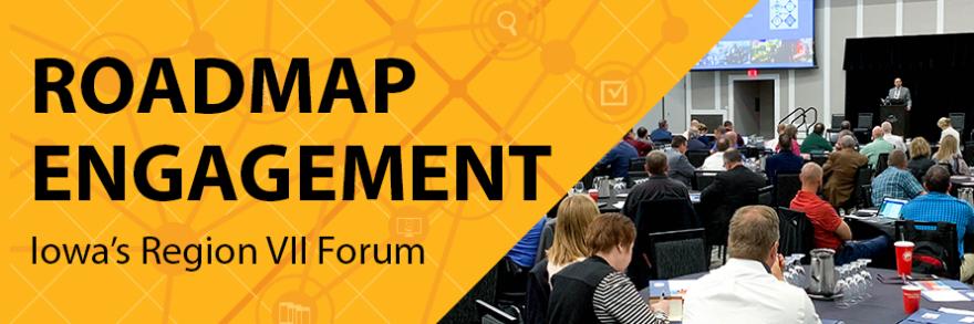 Photograph of event speaker seated in front of crowd of attendees sitting at tables. 