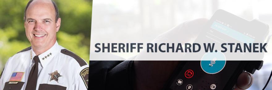 On left, headshot of Sheriff Richard Stanek in uniform, on right, a hand holds a FirstNet device with an app on it