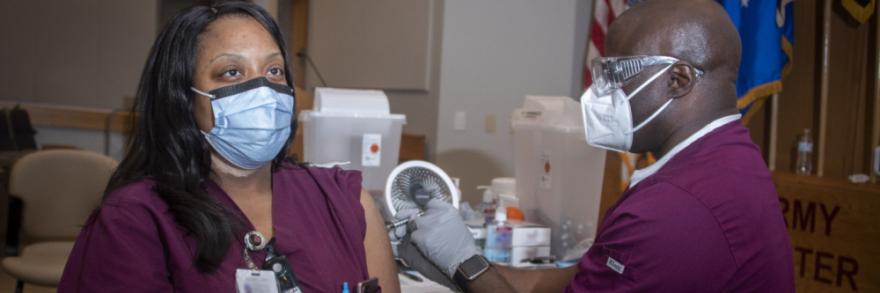 Nurse receives vaccine from her coworker, both are wearing masks