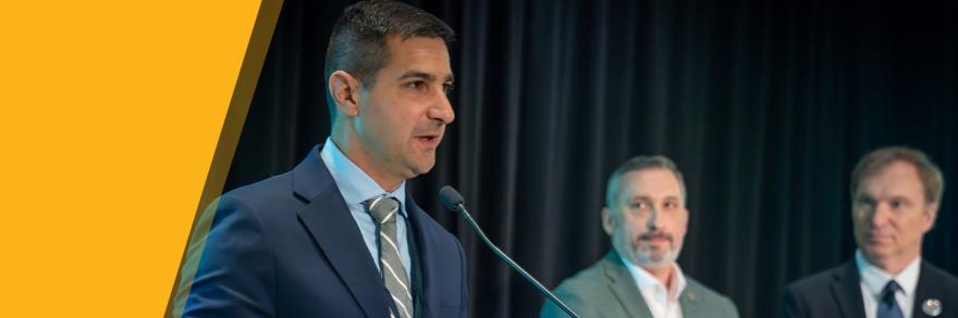 Chief Peter Burke of the Hyannis Fire Department in Massachusetts stands behind podium giving acceptance speech for the inaugural FirstNet Authority Patriot Award; FirstNet Authority Chief Market Engagement Officer Jeremy Zollo and Executive Director / CEO Joe Wassel look on