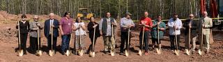 Thirteen people stand with gold shovels, ready to break ground on a cell tower at Red Cliff Reservation