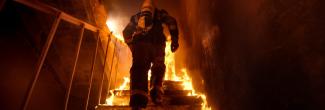 A firefighter ascends a flaming stairwell