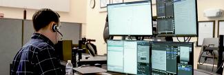 911 operator wearing a headset at a workstation with multiple screens