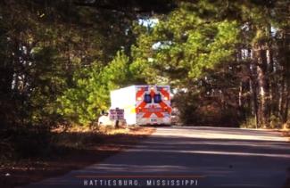 An ambulance drives down a small road on a sunny day. 