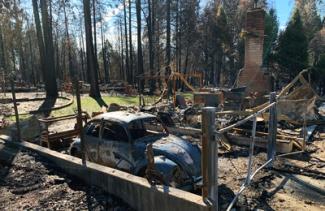A VW bug sits inside the ruins of a burned down house and garage.