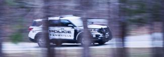 A Farmville Police Department sport utility vehicle driving down the road, captured through the trees.