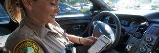A female police officer sits in a patrol car looking at a cell phone.