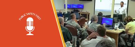Emergency Manager addresses group of individuals including military uniformed men gesturing urgently.