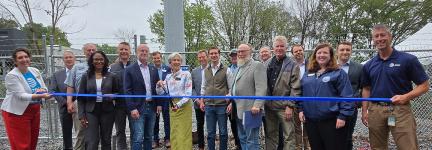FirstNet Authority Executive Director and CEO Michael Cannon stands with federal, state and local leaders in front of a new cell tower with a blue ribbon in front. The mayor in the middle stands ready with scissors to cut the ribbon.