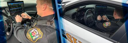 An officer in a Loudoun County Sheriff’s Office uniform sits at a steering wheel of a police vehicle using a mobile data computer mounted to the center console.