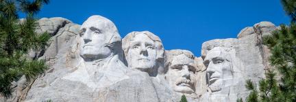 Framed on either side by tree branches, Mount Rushmore from below on a clear day with no clouds.