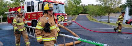 Two firefighters from the Toms River Fire Department in New Jersey carry a ladder while walking on a street in front of a fire truck