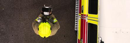 Aerial view of a firefighter wearing a helmet using a drone next to a firetruck